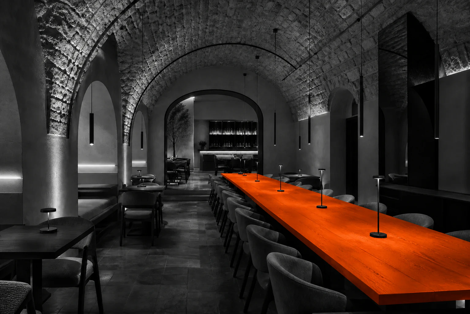 Monochrome restaurant inside historic stone vaults with a saturated orange communal table